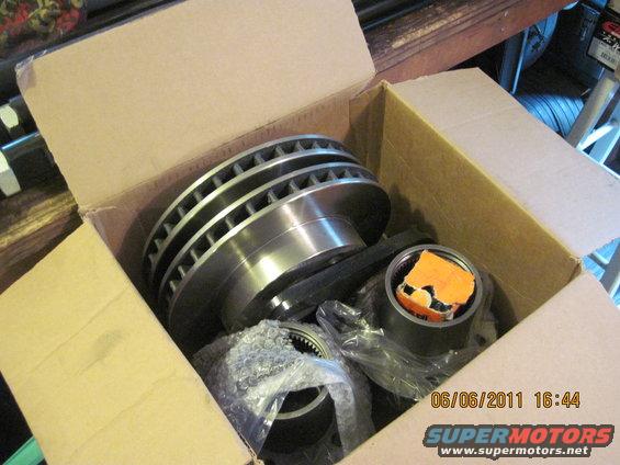 Box of new brake rotors and other car parts, some wrapped in plastic