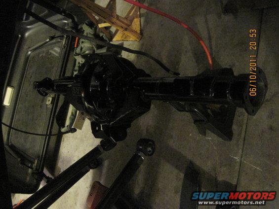 Black rear axle assembly with suspension components attached, lying on concrete floor