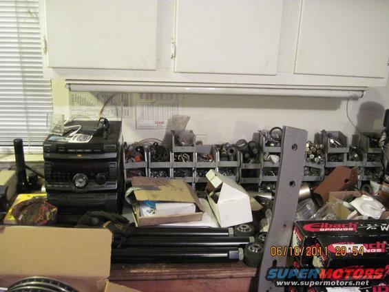 Workbench with stereo, bins of parts, and boxes. Some parts are labeled Eibach Springs