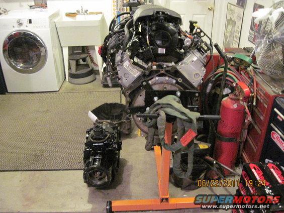 Engine and transmission on stands in a garage with a washing machine and sink