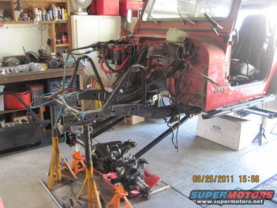 1985 Jeep CJ7 body on jack stands, front end disassembled, engine bay exposed, in a garage