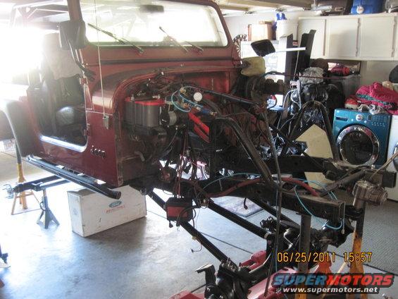Red Jeep CJ7 body on jack stands, engine removed, showing frame and suspension