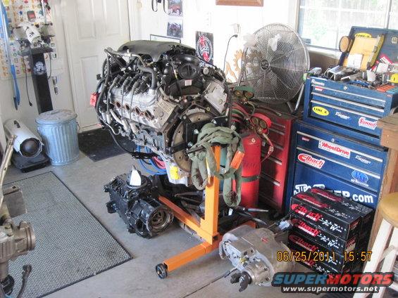 Engine on an orange engine stand in a garage with toolboxes and a fan
