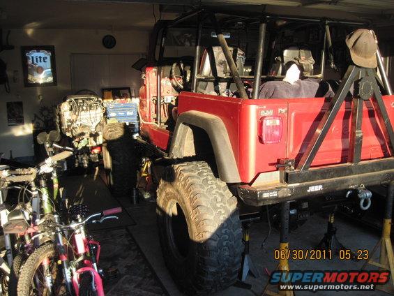 Red Jeep with roll cage and large tires, jacked up in a garage