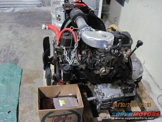 Engine and transmission assembly on a wooden pallet, with a box of parts nearby. Date stamp reads 06/30/2011