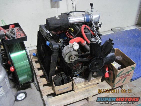 Engine assembly with air filter, radiator, and fan, sitting on a pallet next to a welding cart