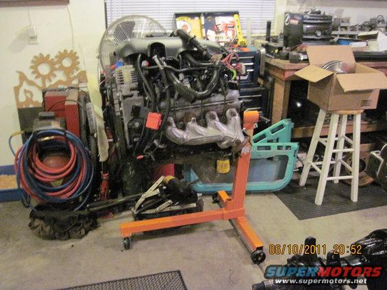 Engine on an orange engine stand in a garage, with tools and parts in the background