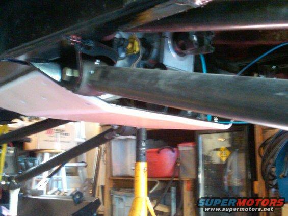 Underside of a vehicle with suspension components and a skid plate visible. It's on jack stands in a garage