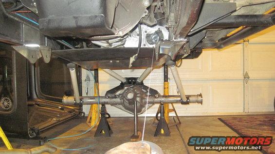 Undercarriage of a vehicle on jack stands, showing the rear axle assembly and suspension components