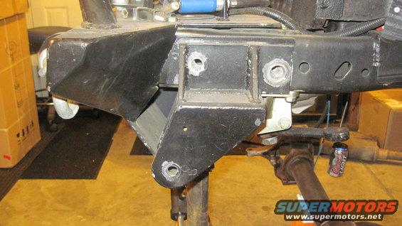 Close-up of a modified Jeep CJ frame with custom brackets and suspension components. A can of Coors Light is visible
