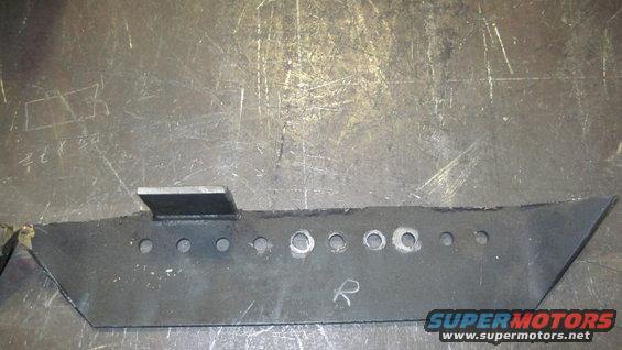 Fabricated metal bracket with multiple holes and a welded tab, resting on a metal surface