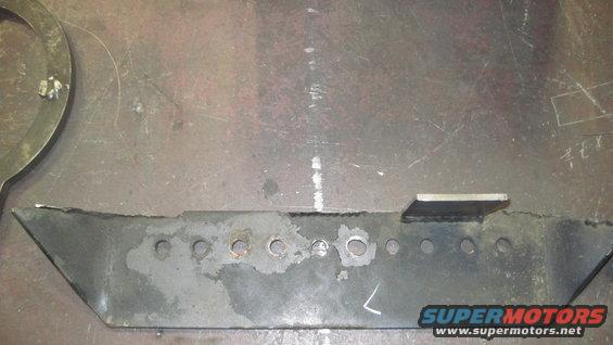 metal bracket with multiple holes and a welded tab, on a workbench