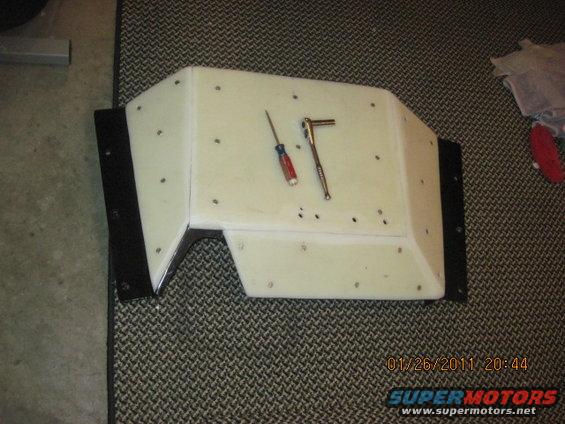 White fiberglass automotive part with black trim, on a patterned carpet. A screwdriver and ratchet are on top