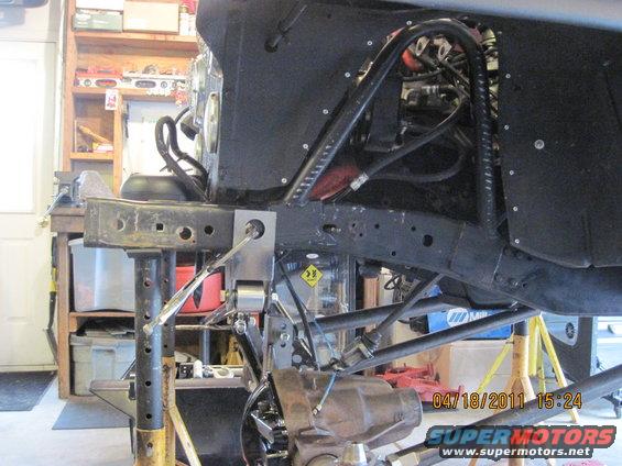 Close-up of a Jeep's frame and suspension system with hydraulic lines and a differential visible. The vehicle is supported by jack stands