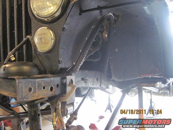 Front wheel well and frame of a Jeep, possibly undergoing repairs. Headlight and grille visible
