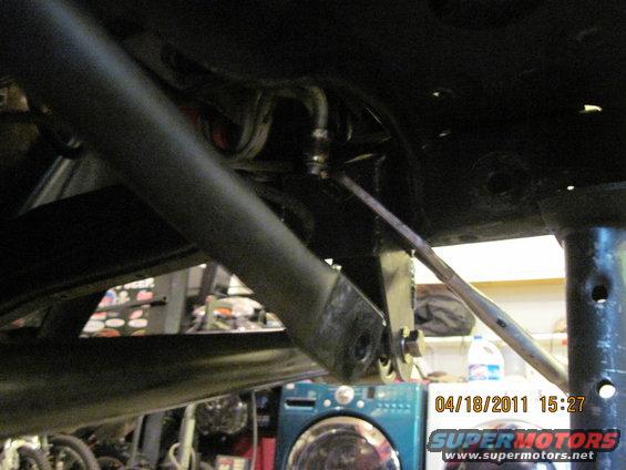 Undercarriage of a vehicle with a large black bar and metal linkage, viewed from below