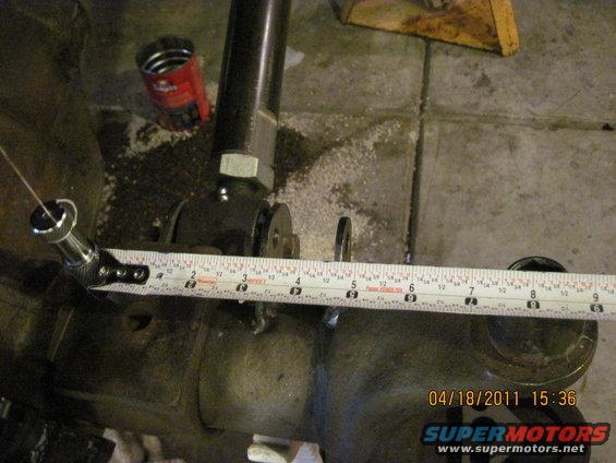 Measuring a vehicle axle housing with a tape measure. A red can is visible in the background