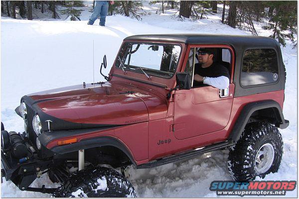 1985 Jeep CJ7 in snow with driver. "Jeep" badge visible on side