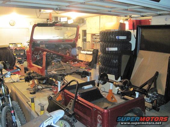Red Jeep CJ body disassembled in garage, parts scattered around