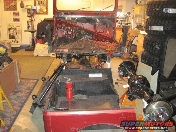 1985 Jeep CJ7 disassembled in a garage, showing the interior and chassis. A rear axle assembly is on an orange stand