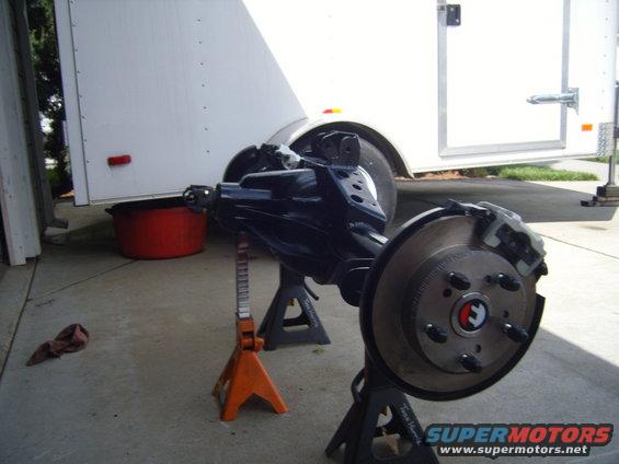 Jeep rear axle assembly with disc brakes on jack stands, next to a white trailer