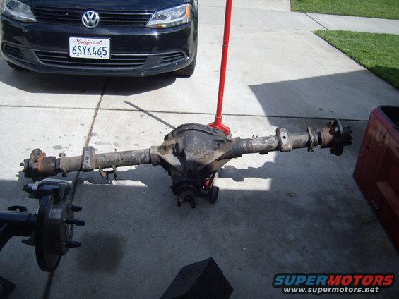 Rear axle assembly on concrete with black Volkswagen Jetta in background