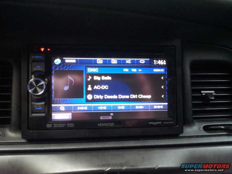 Car interior showing aftermarket Kenwood stereo display with music track list