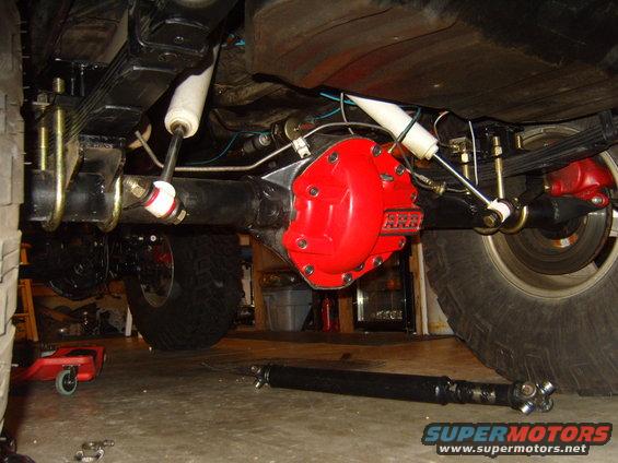 Jeep rear axle assembly with red differential cover and leaf springs. Driveshaft is on the floor