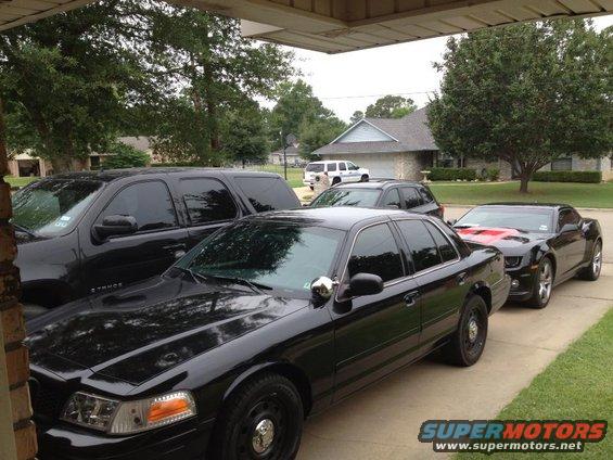 2007 Ford Crown Victoria police car parked next to a black Chevrolet Camaro and a black SUV