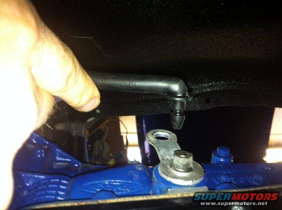 hand pointing to a black hose connected to a metal bracket on a blue painted part of a vehicle