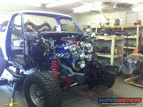 White Ford Bronco body with engine exposed, lifted on a jack, in a workshop