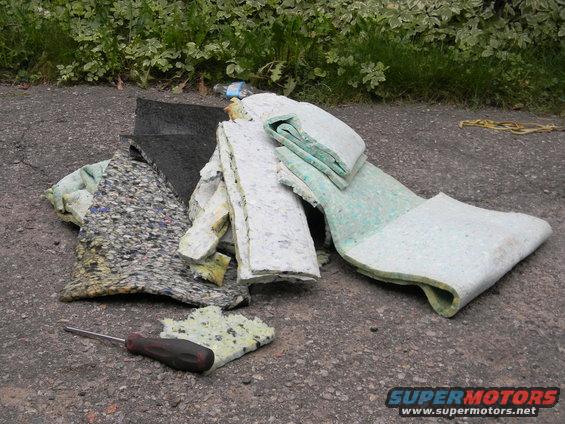 Pile of foam padding and carpet scraps on asphalt, with a screwdriver nearby