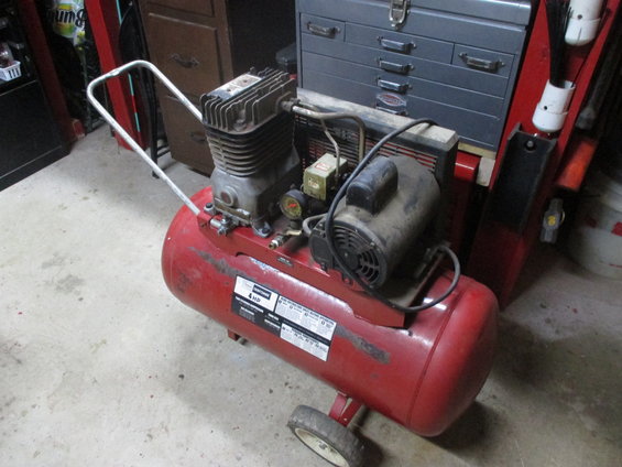 Red air compressor with a silver handle and a black motor, seen from a 3/4 front angle in a workshop