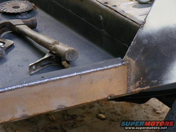 Hammer and cutting disc on a metal surface, possibly a vehicle frame undergoing repair. Welds are visible