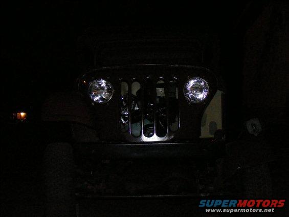 Front view of a Jeep CJ-5 grille with aftermarket headlights at night