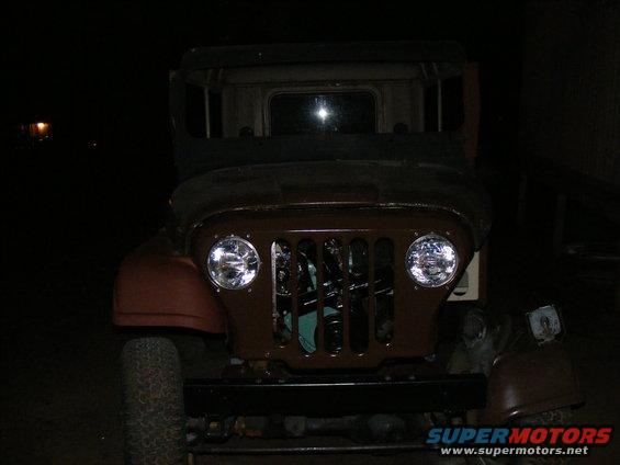 Front view of an old Jeep with a brown grille and round headlights. The vehicle appears to be undergoing restoration