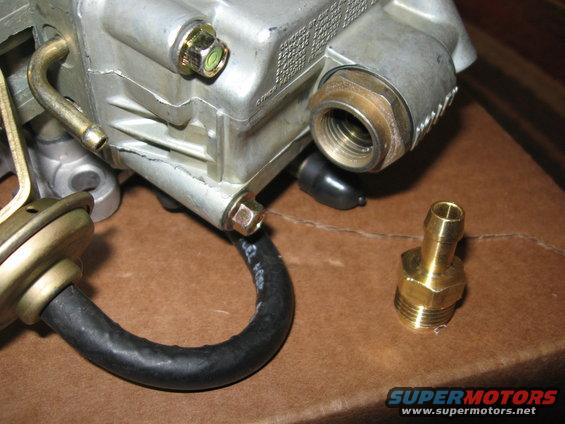 Carburetor with brass fitting and black hose on brown surface