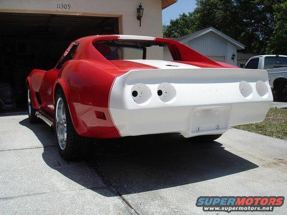 1976 Chevrolet Corvette, red with white racing stripes, parked outside a garage