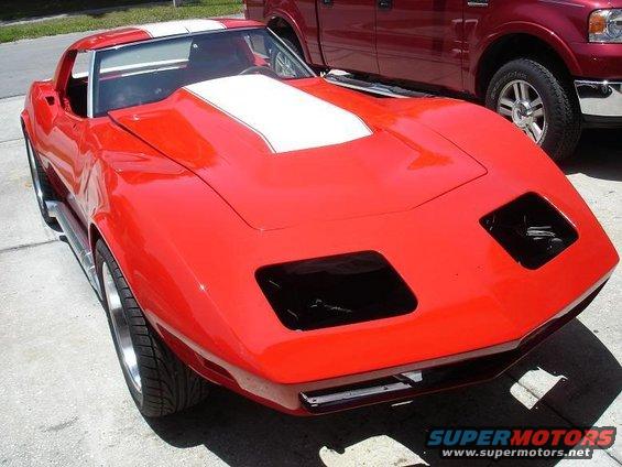 Red Chevrolet Corvette with white hood and roof stripes, missing headlights, parked next to a red pickup truck