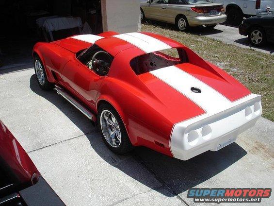 Red Chevrolet Corvette with white racing stripes, seen from the rear three-quarter angle, parked on a concrete driveway
