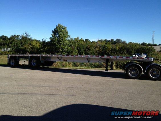 Flatbed trailer parked on asphalt with trees and blue sky in background
