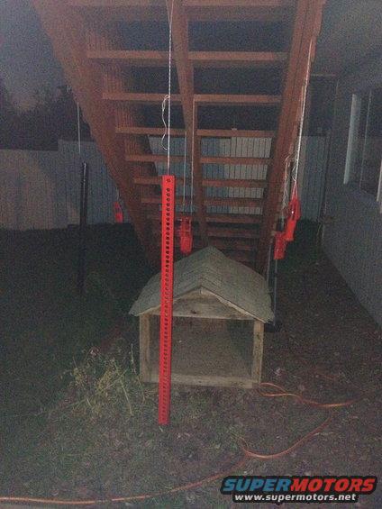 Red Hi-Lift jack leaning against a wooden dog house under stairs