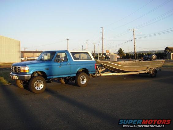 Blue 1995 Ford Bronco with a white top, lifted, towing a boat on a trailer
