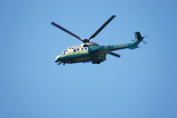 Sheriff helicopter flying in a clear blue sky. It is green and white with 'SHERIFF' written on the side