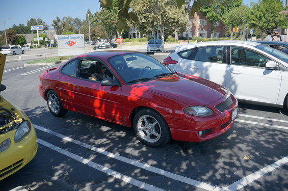 Red coupe parked in a lot next to a yellow car and a white car