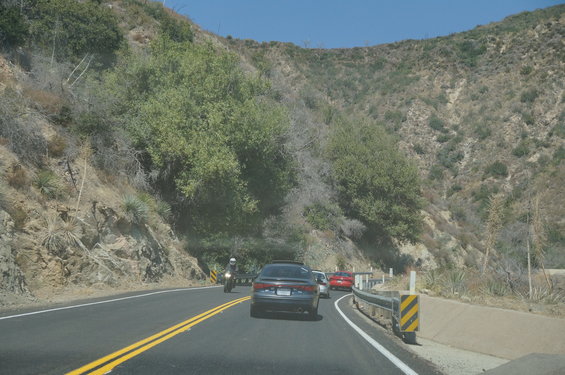 Dark sedan seen from behind on a winding road with a motorcycle and other cars
