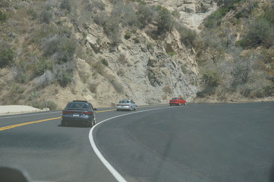 Three cars driving on a two-lane road next to a rocky hillside