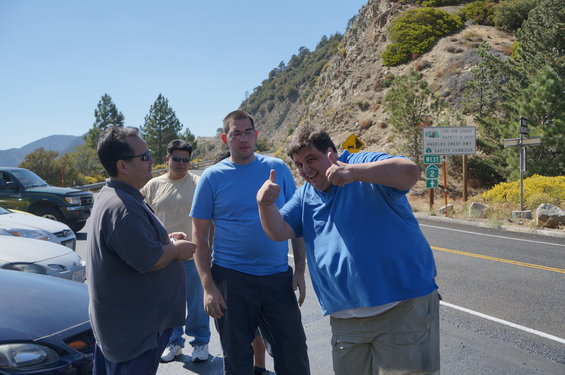 Group of men with cars parked on a mountain road, sign for Angeles Crest Highway