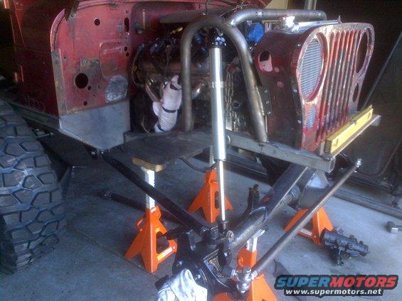 Red Jeep CJ front end on jack stands, showing engine and suspension components