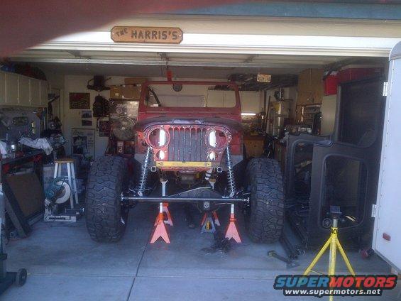 1985 Jeep CJ7 front end on jack stands in garage, disassembled. Front grille, headlights, and suspension visible